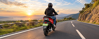 Rider on an Odysse scooter along a coastal road at sunset